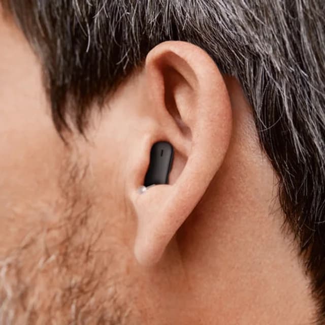 Close-up of an ear with a small black in-canal hearing aid sitting deep in the canal, barely visible